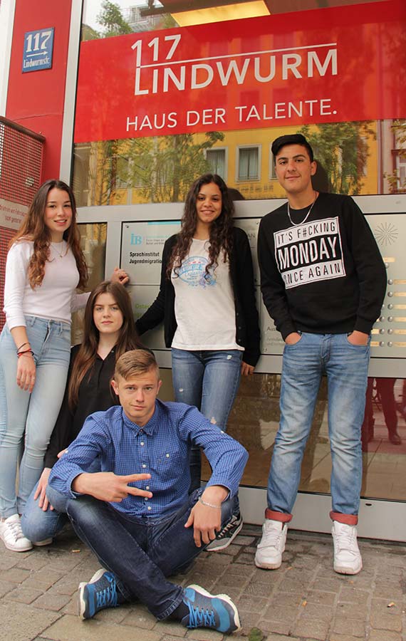 Sechs Jugendliche posieren vor dem Gebäude mit der Aufschrift '117 LINDWURM HAUS DER TALENTE'. Zwei stehen, vier sitzen, einer zeigt das Peace-Zeichen.